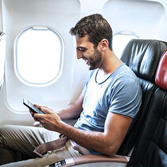 棕色头发的男子坐在飞机上靠窗的位置，用智能手机上网