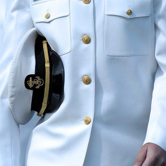 一个身穿白色海军制服，胳膊下夹着海军帽子的男人的特写镜头