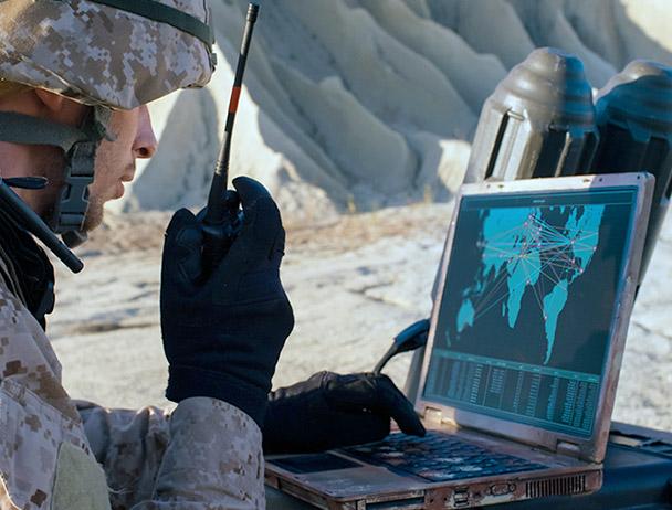 一名士兵对着手提卫星收音机说话，看着笔记本电脑上的地图