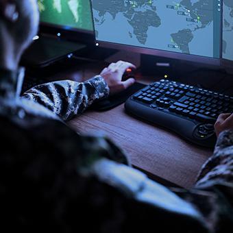 一名军人坐在台式电脑前，看着显示器上的世界地图
