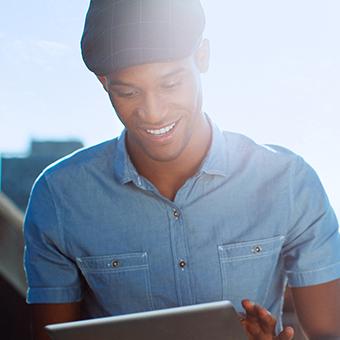 一名身穿蓝色纽扣衬衫、头戴平顶帽的男子对着平板电脑微笑