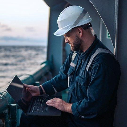 戴安全帽的男子在海上的船上用笔记本电脑上网.
