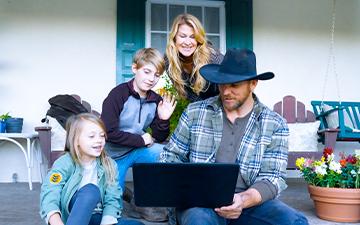 一个牧场主，他的妻子和两个孩子在门廊上用他们的笔记本电脑享受家庭wifi