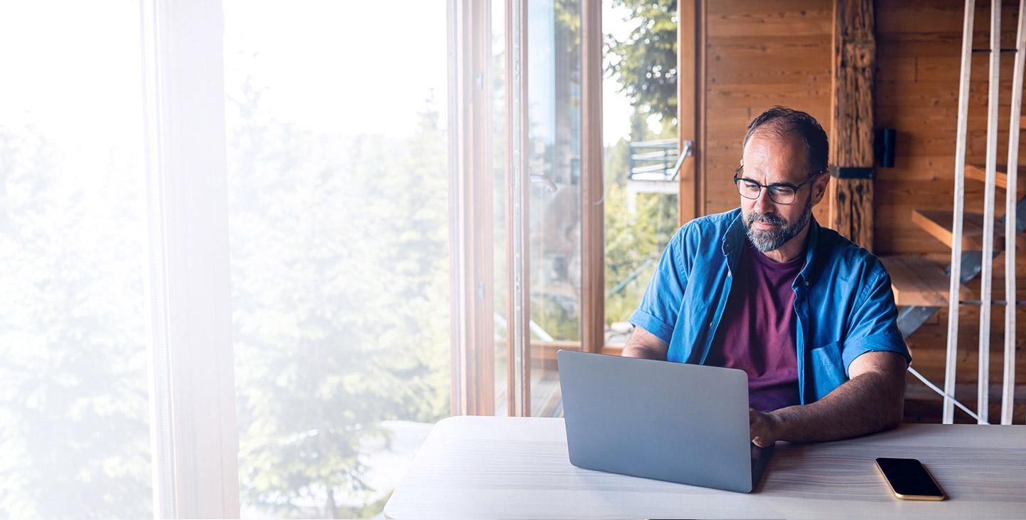 一个拥有家庭无线网络计划的男人坐在他山上房子的桌子上用笔记本电脑 